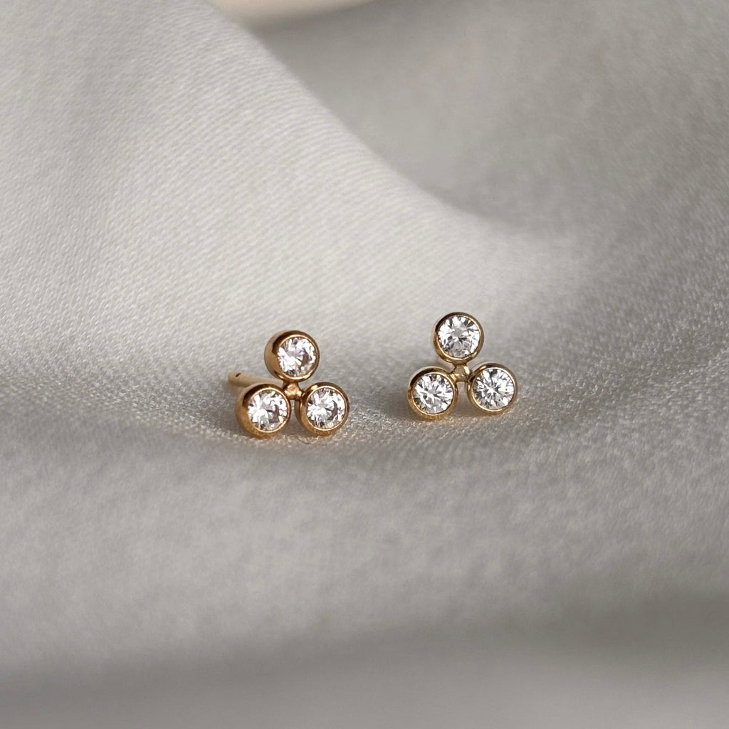 Close-up of delicate triple cluster bezel set cubic zirconia stud earrings on a soft fabric background
