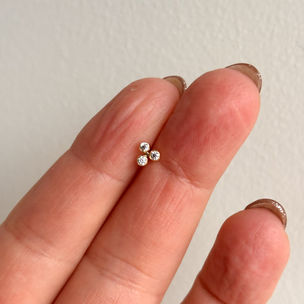 Small diamond stud earring held between two fingers against a plain background